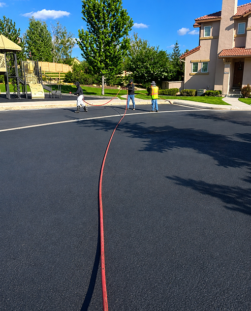 Prime Line Company crew applying professional asphalt sealcoating to a residential community roadway in Colorado